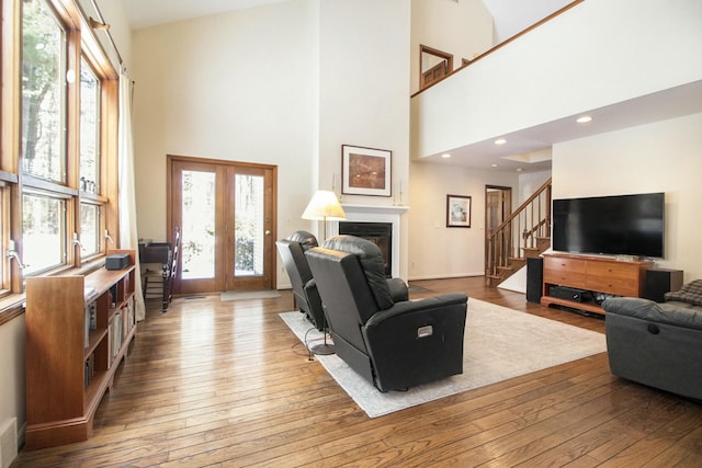 living area featuring a glass covered fireplace, wood finished floors, stairs, french doors, and recessed lighting