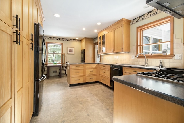 kitchen featuring dark countertops, light brown cabinetry, glass insert cabinets, a sink, and black appliances