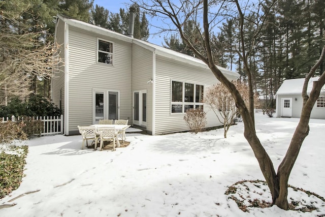 snow covered house featuring an outdoor structure and fence