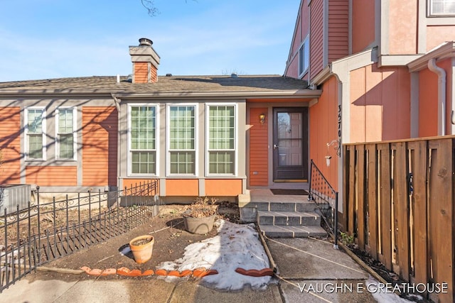 view of exterior entry with a chimney and fence