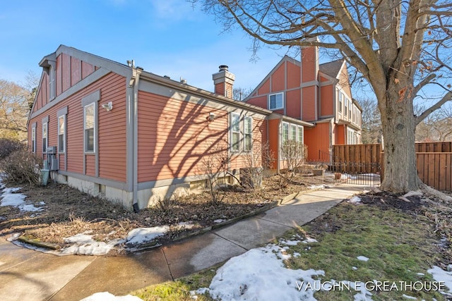 view of snowy exterior with a chimney and fence