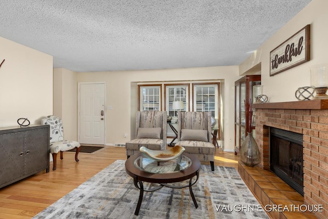 living area featuring a textured ceiling, a fireplace, wood finished floors, and baseboards