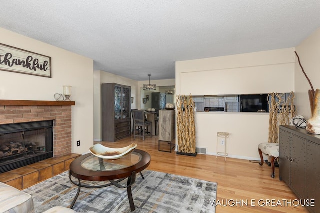 living room featuring a brick fireplace, visible vents, a textured ceiling, and wood finished floors