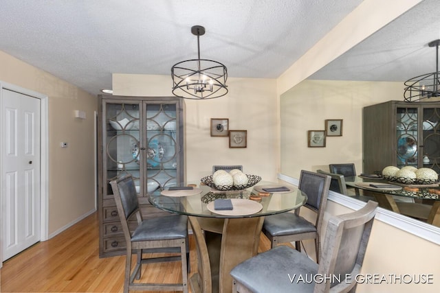 dining space with light wood finished floors, a textured ceiling, and a notable chandelier