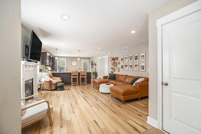 living area with light wood finished floors, recessed lighting, visible vents, and a glass covered fireplace