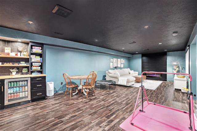 interior space with a textured ceiling, wine cooler, wood finished floors, visible vents, and baseboards