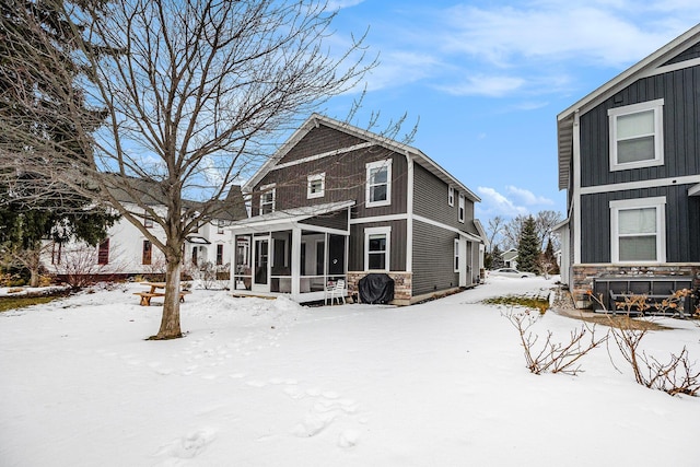 snow covered rear of property with a sunroom