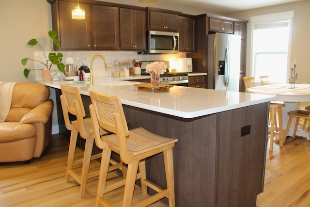 kitchen featuring light countertops, hanging light fixtures, appliances with stainless steel finishes, a peninsula, and a kitchen breakfast bar