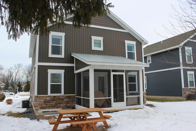 snow covered rear of property featuring stone siding and a sunroom