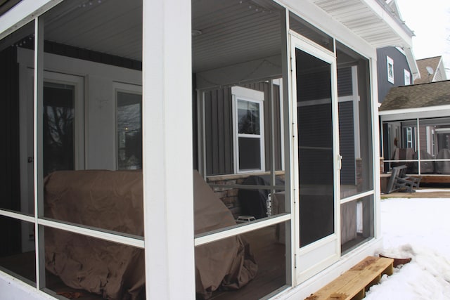 view of snowy exterior with a sunroom, stone siding, and roof with shingles