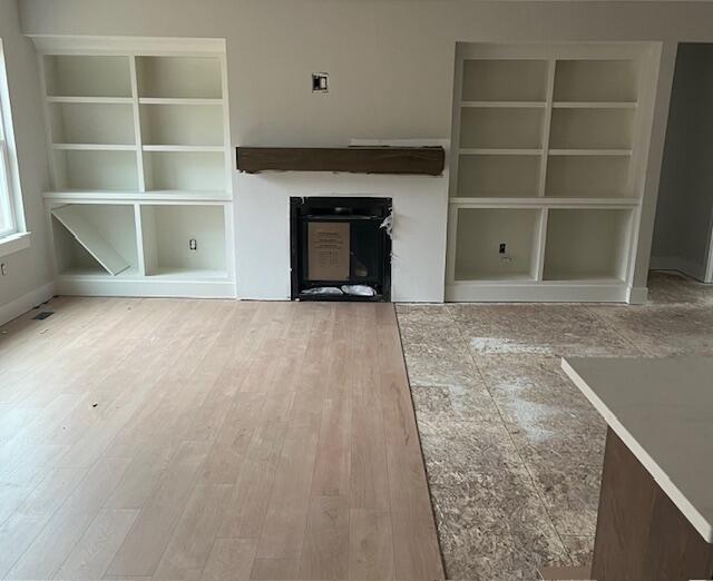 unfurnished living room with a fireplace, wood finished floors, and built in features