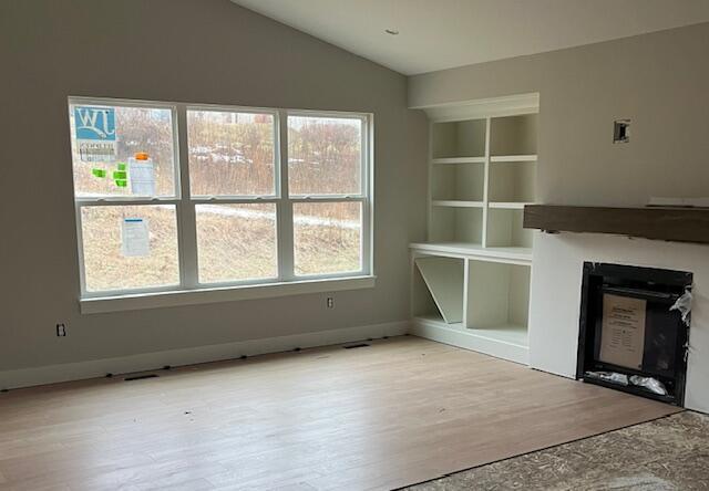 unfurnished living room featuring lofted ceiling, a fireplace, baseboards, and wood finished floors