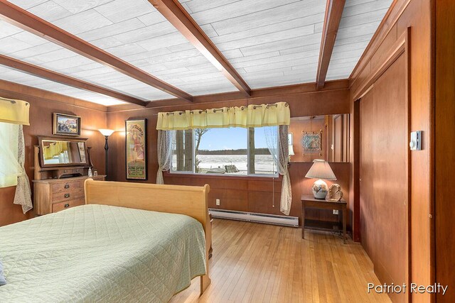 bedroom with a baseboard heating unit, hardwood / wood-style floors, wood walls, and beam ceiling