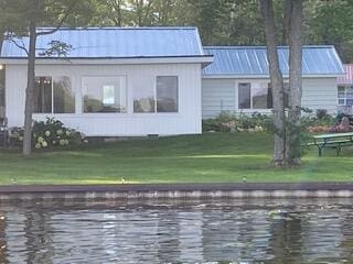 rear view of property featuring metal roof, a water view, and a yard