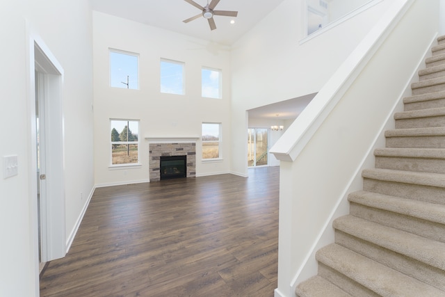 unfurnished living room with baseboards, a towering ceiling, stairway, dark wood-style flooring, and ceiling fan with notable chandelier