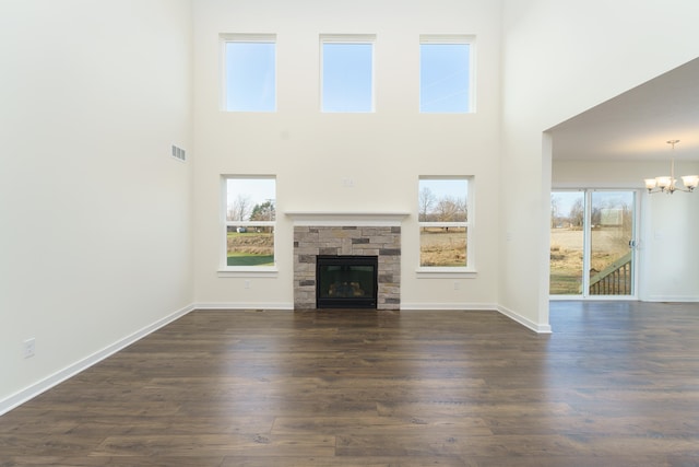 unfurnished living room featuring dark wood-style flooring, visible vents, a stone fireplace, a chandelier, and baseboards