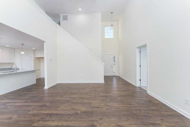 unfurnished living room with a sink, dark wood finished floors, a towering ceiling, and baseboards