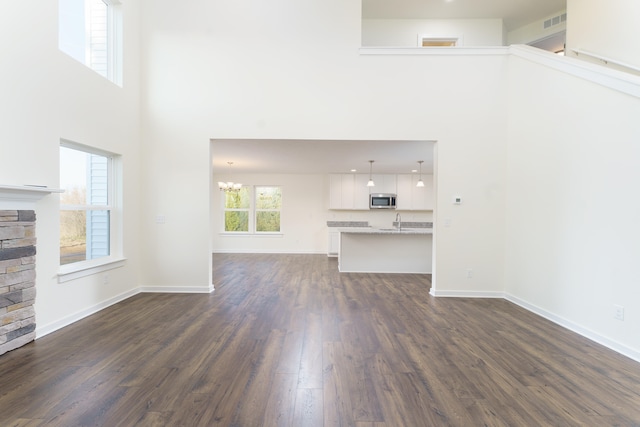 unfurnished living room with dark wood-style floors, a sink, baseboards, and an inviting chandelier