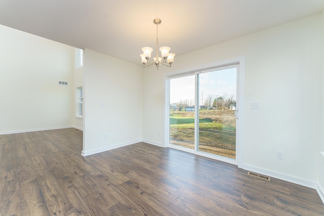 empty room with dark wood-style floors, visible vents, a notable chandelier, and baseboards