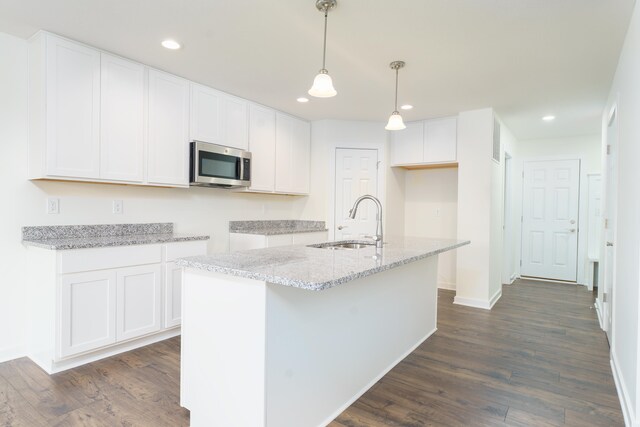 kitchen featuring a sink, white cabinetry, stainless steel microwave, decorative light fixtures, and an island with sink