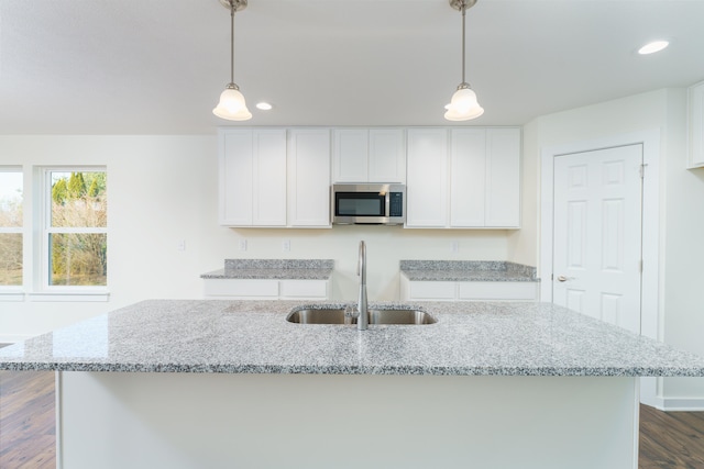 kitchen featuring light stone countertops, white cabinetry, stainless steel microwave, and a sink