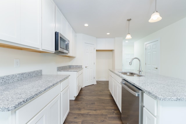 kitchen featuring decorative light fixtures, a sink, white cabinets, appliances with stainless steel finishes, and a center island with sink