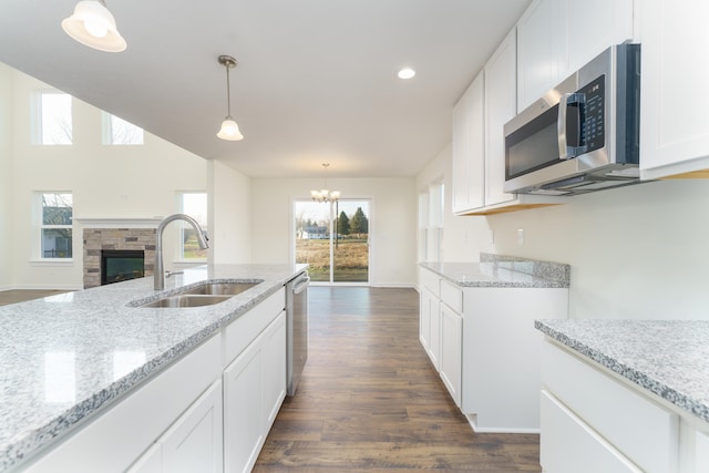 kitchen with stainless steel appliances, a sink, white cabinets, hanging light fixtures, and light stone countertops