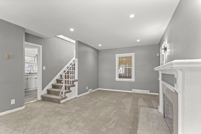 unfurnished living room with light carpet, a tile fireplace, stairs, and baseboards