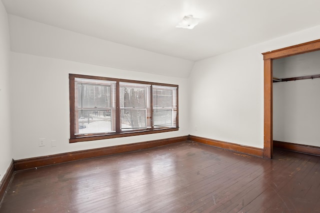 unfurnished bedroom with vaulted ceiling, a closet, wood-type flooring, and baseboards