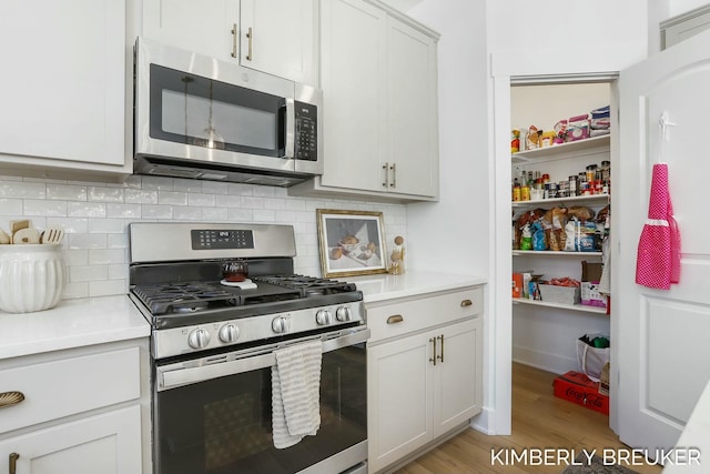 kitchen with light wood-style flooring, white cabinets, light countertops, appliances with stainless steel finishes, and decorative backsplash