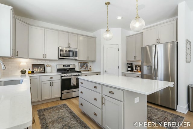 kitchen featuring a center island, light countertops, gray cabinetry, appliances with stainless steel finishes, and a sink