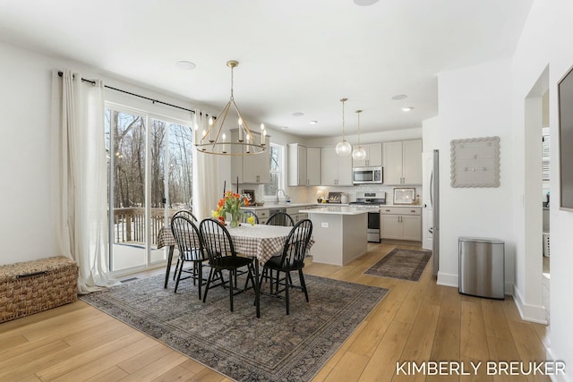 dining room with light wood-type flooring, a notable chandelier, and baseboards