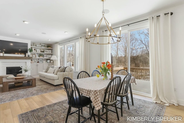 dining room featuring light wood finished floors, recessed lighting, a chandelier, and a glass covered fireplace