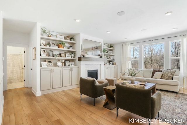 living area with light wood-style floors, recessed lighting, and a glass covered fireplace