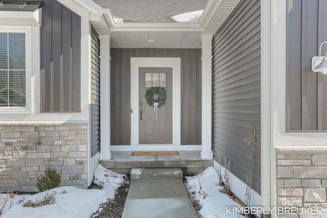 snow covered property entrance featuring stone siding and a shingled roof