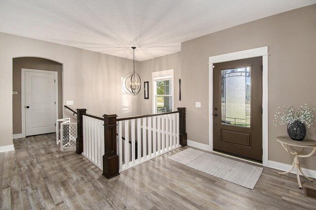 entrance foyer with a chandelier, arched walkways, wood finished floors, and baseboards