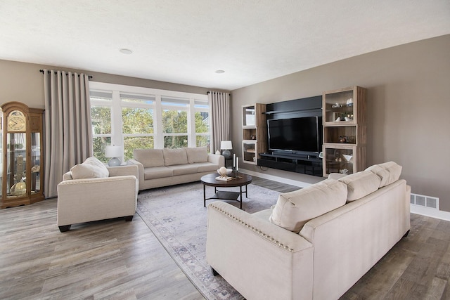 living room with a textured ceiling, wood finished floors, visible vents, and baseboards