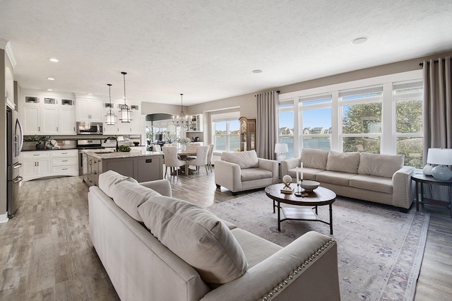 living room with a textured ceiling, a water view, wood finished floors, and a notable chandelier