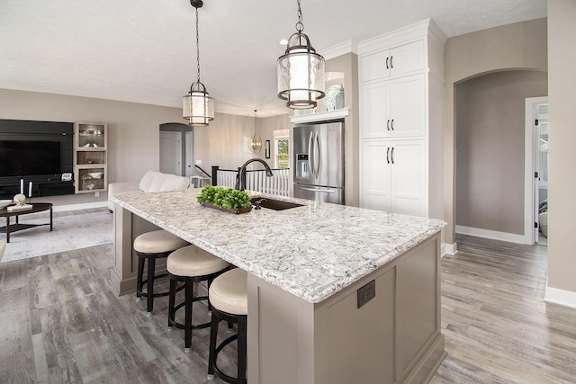 kitchen with arched walkways, white cabinetry, a large island, stainless steel fridge, and decorative light fixtures