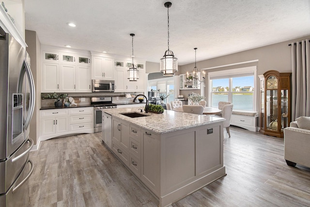 kitchen with a water view, a sink, white cabinets, appliances with stainless steel finishes, and glass insert cabinets