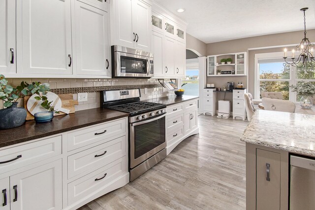 kitchen with white cabinets, decorative backsplash, glass insert cabinets, stainless steel appliances, and pendant lighting