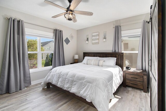 bedroom featuring a ceiling fan, light wood-type flooring, baseboards, and a barn door