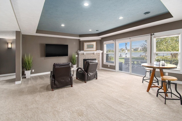 living area with baseboards, light colored carpet, a tray ceiling, a textured ceiling, and a fireplace