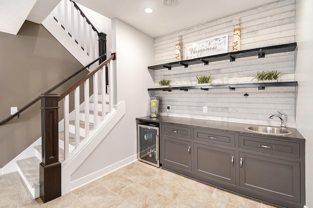 bar with a sink, beverage cooler, bar, baseboards, and stairs