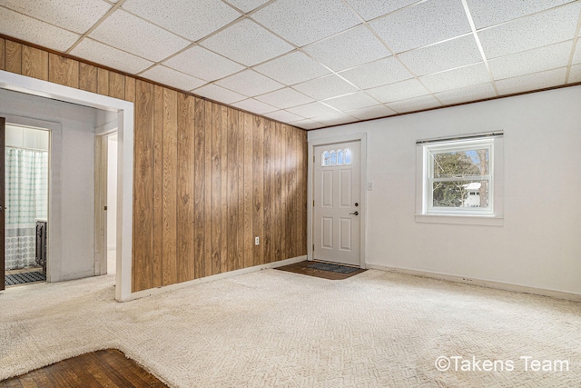 carpeted entryway with baseboards, a drop ceiling, and wooden walls