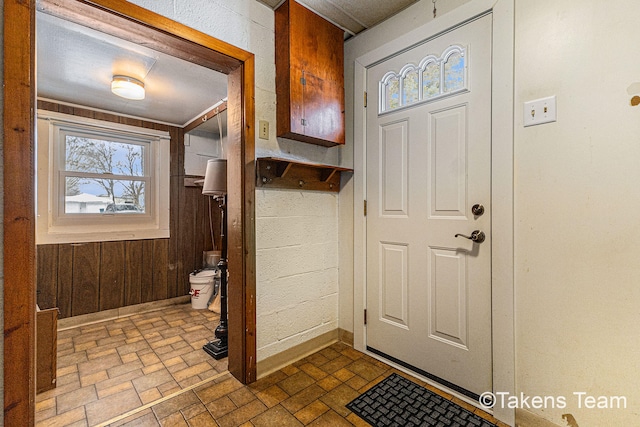 entryway featuring brick floor, wood walls, and baseboards