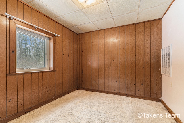 empty room with light colored carpet, visible vents, wood walls, and baseboards