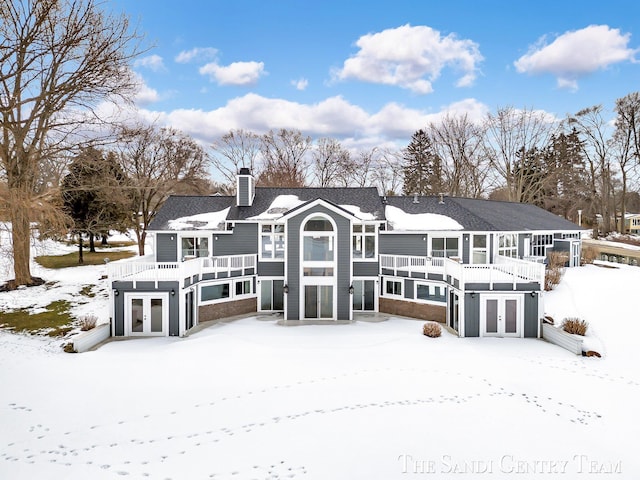 snow covered property with french doors, a chimney, and a balcony