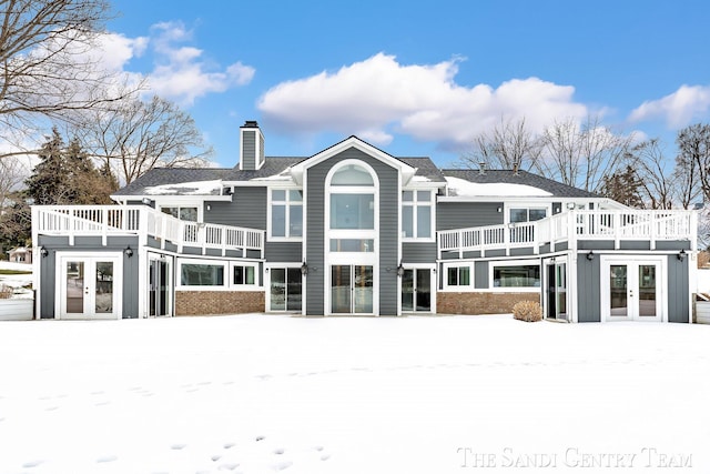 snow covered house featuring french doors, brick siding, and a chimney