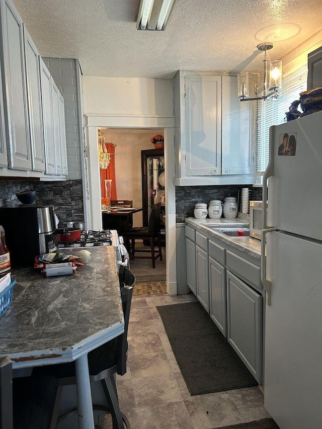 kitchen featuring tasteful backsplash, a breakfast bar, decorative light fixtures, freestanding refrigerator, and white cabinetry